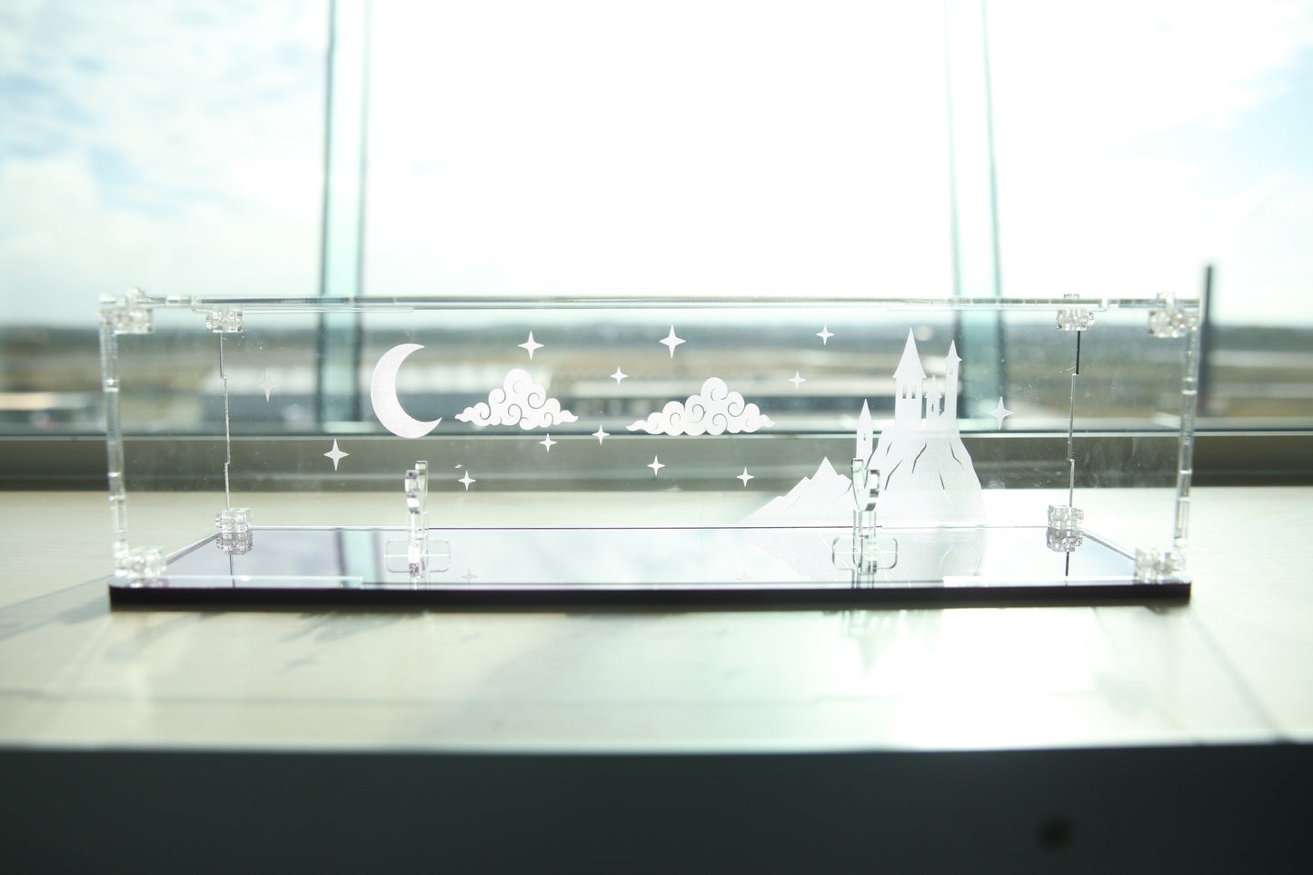 Clear acrylic wand display case with coloured base and fantasy castle and sky engraving on the back.