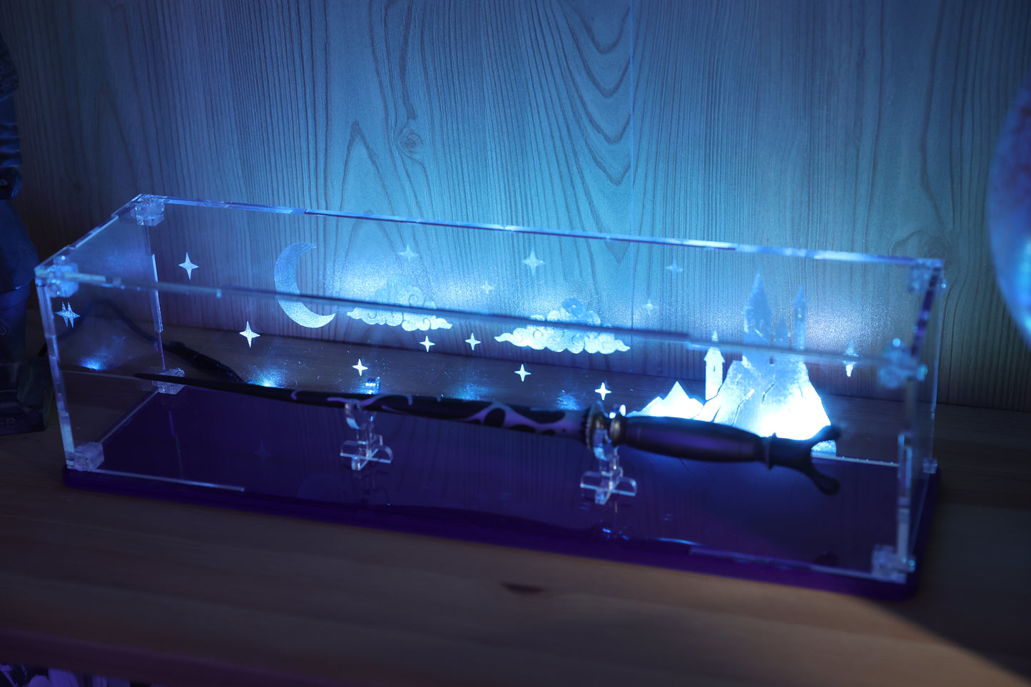 Clear acrylic wand display case with coloured base and fantasy castle and sky engraving on the back.