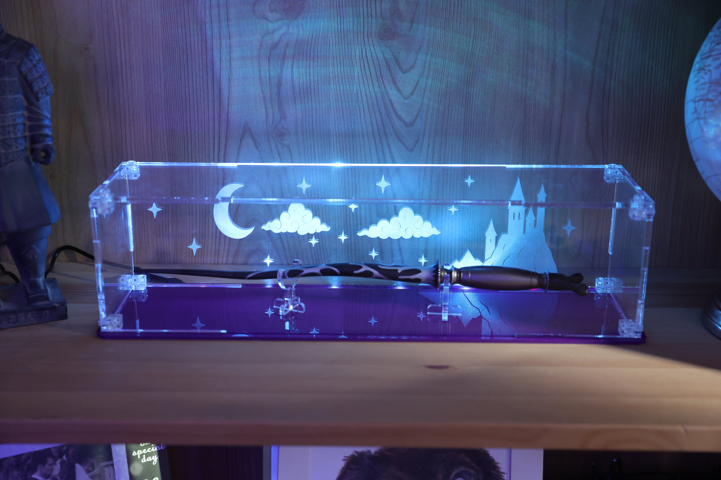 Clear acrylic wand display case with coloured base and fantasy castle and sky engraving on the back.