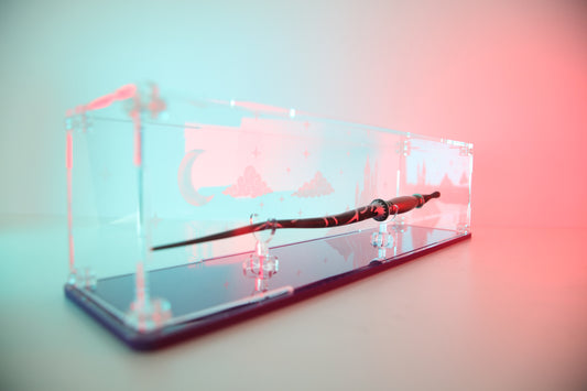 Clear acrylic wand display case with coloured base and fantasy castle and sky engraving on the back.